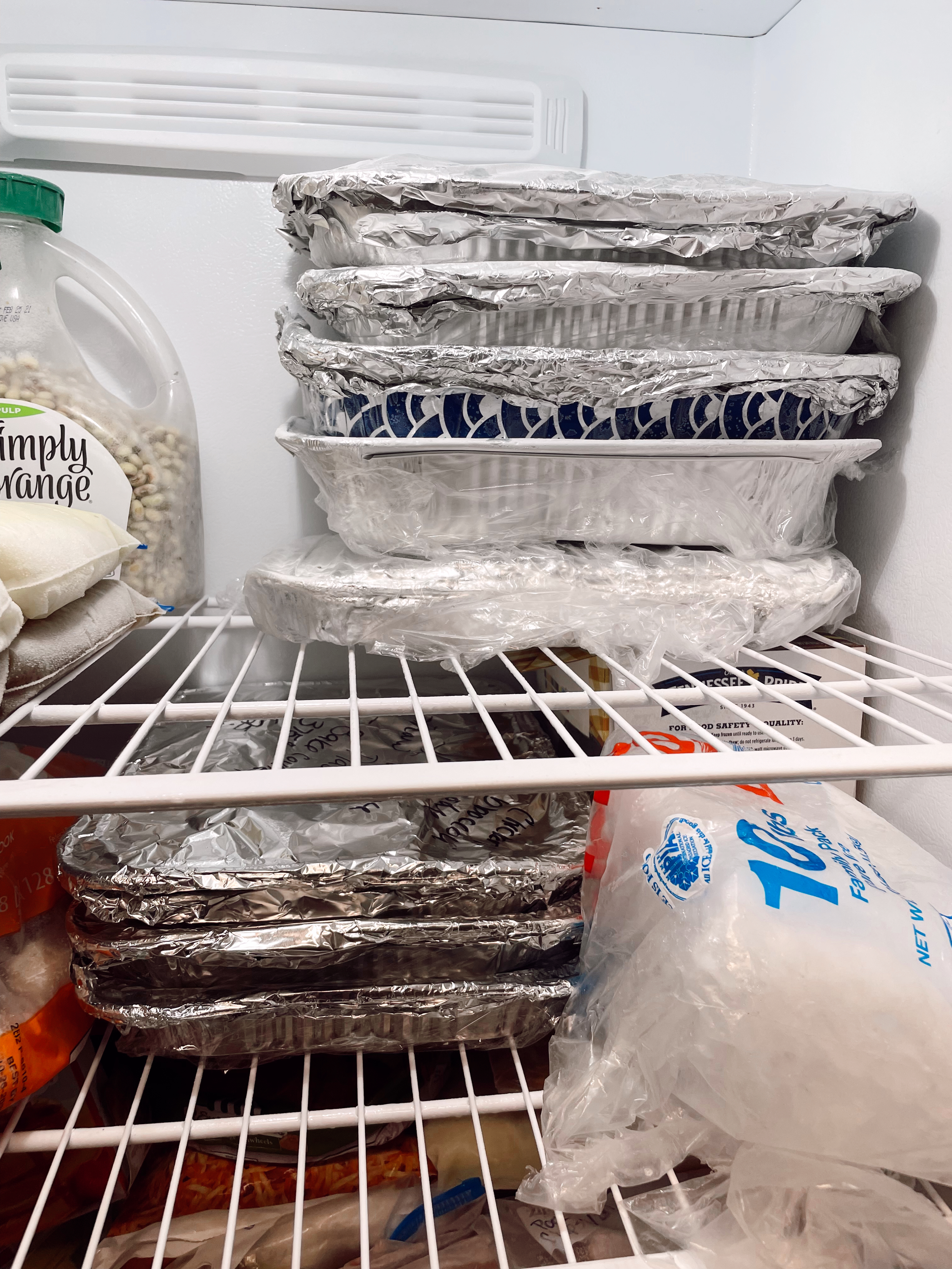 Freezer meals in foil pans in freezer on shelf with various other products. 