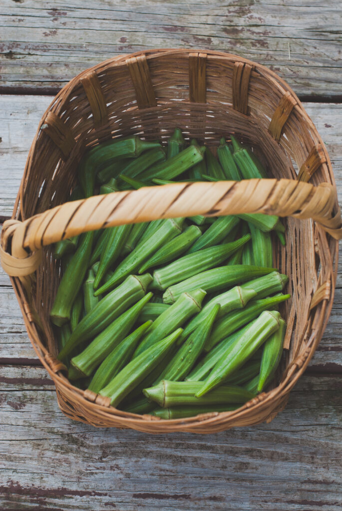 okra pods in a woven basket with brown wood in background 