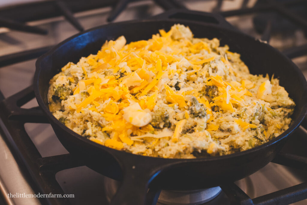 Bread batter in a cast iron skillet with cheese and and broccoli.