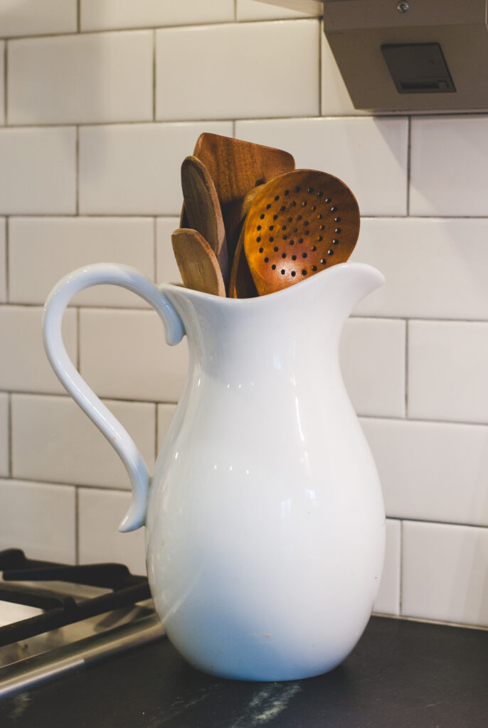 Wooden homestead kitchen tools in white pitcher on counter 