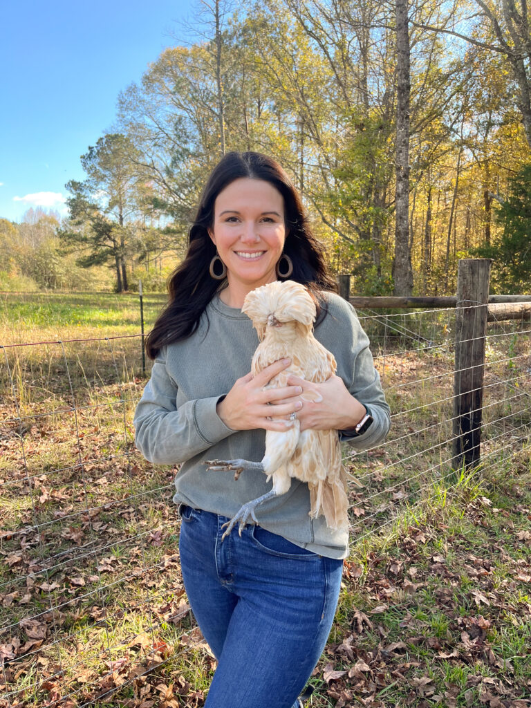 Girl holding chicken while homesteading outside in front of a fence 