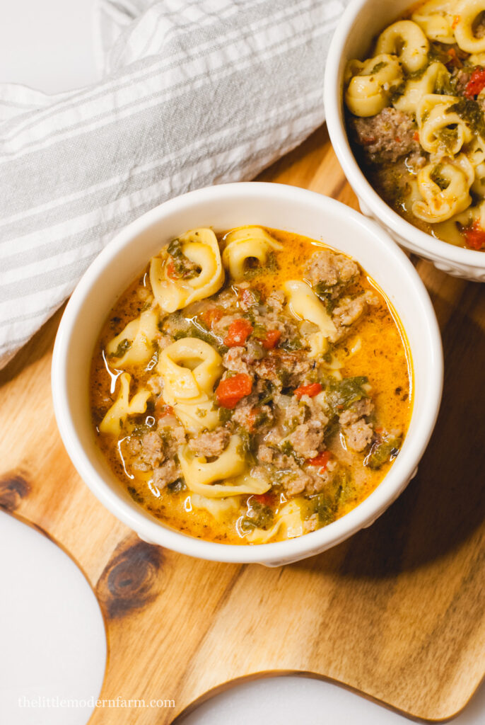 Sausage tortellini soup in a white bowl on a wooden surface 