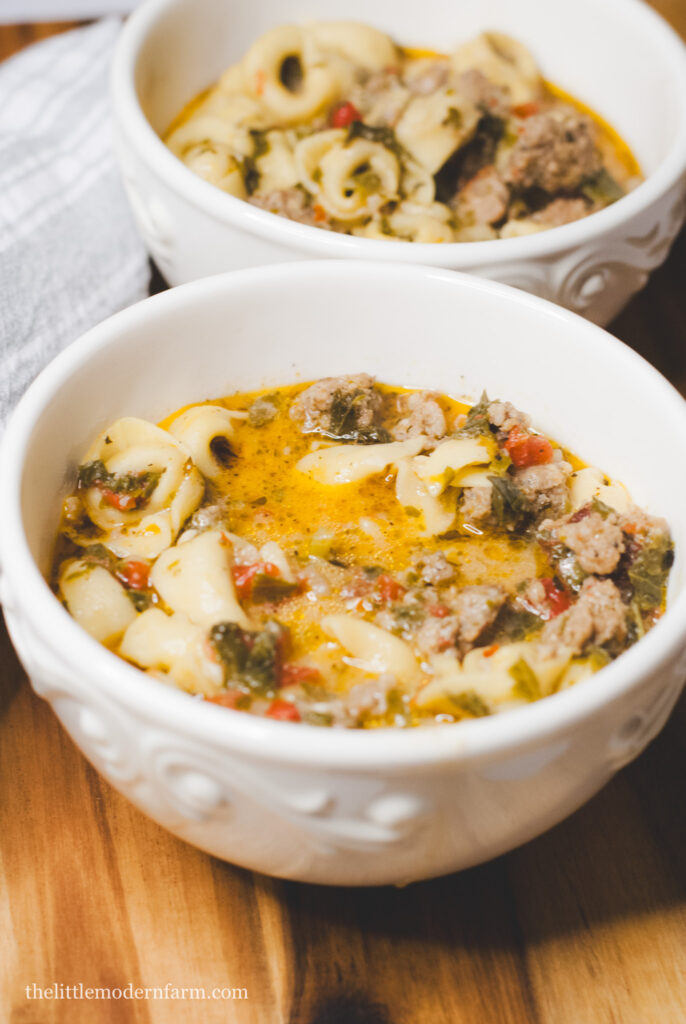 Sausage tortellini soup in a white bowl on a wooden surface 