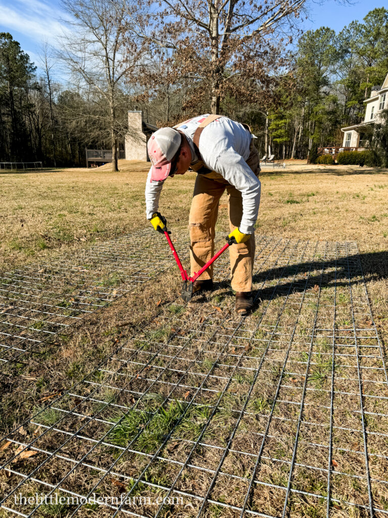 man in overalls cutting a cattle panel with wire cutters 