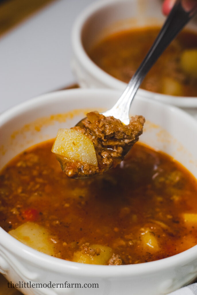 tomato potato soup on a spoon with bowl of soup behind it 