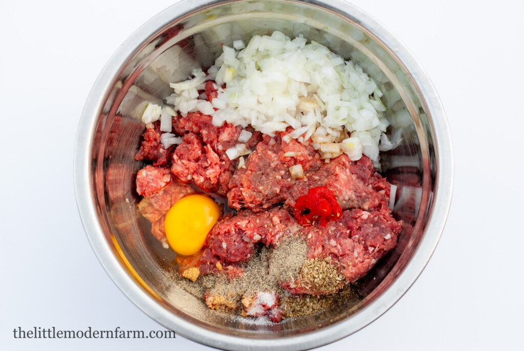 Ground venison, onion, spices, and an egg in a stainless steel bowl 