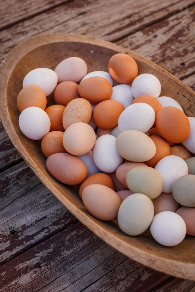 various colored fresh eggs in a wooden bowl. 