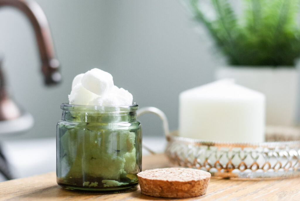 Essential oil bath bomb in a green glass jar on a shelf. 