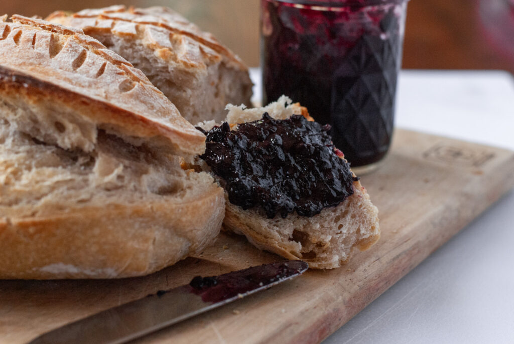 blueberry jalapeño jam on a piece of bread with a jar and a knife 