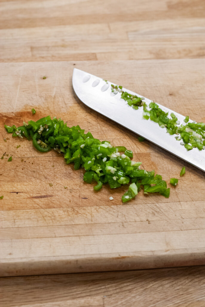 Chopped jalapeños on a cutting board with a knife 