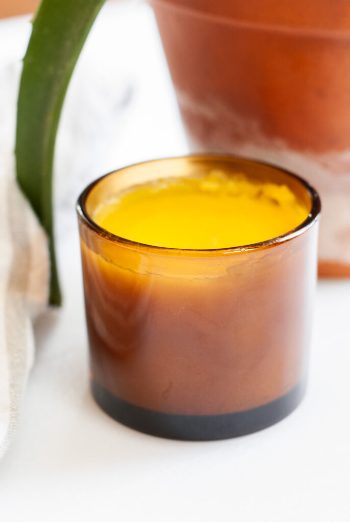 Yellow after sun lotion in an amber jar on a white surface with aloe vera plant. 