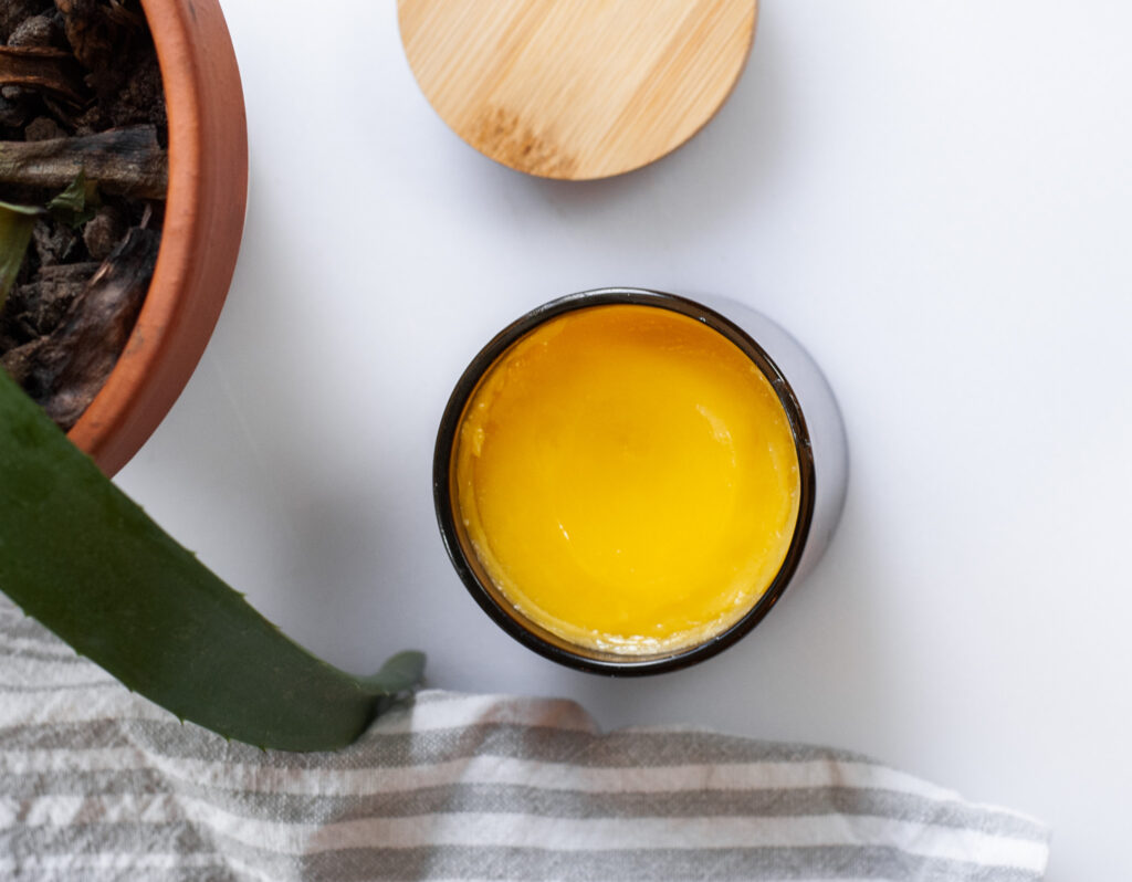 Yellow after sun lotion in an amber jar on a white surface with aloe vera plant. 