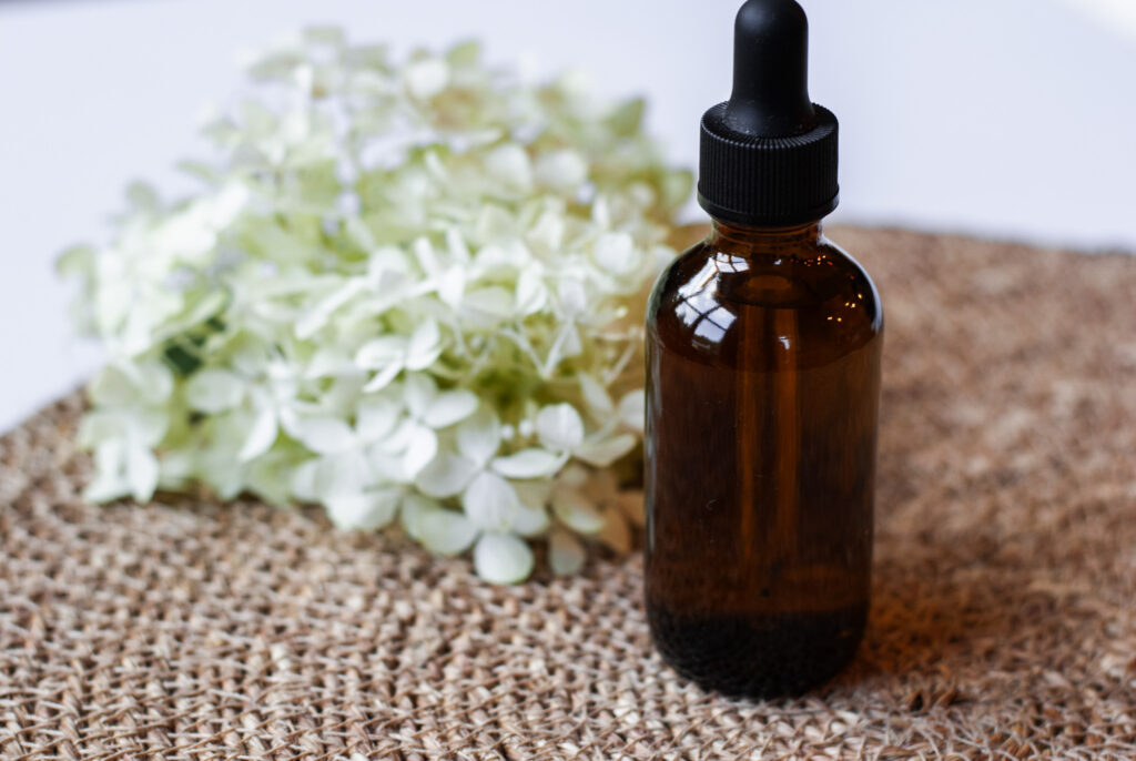 Amber glass jar of eyelash serum next to flower 