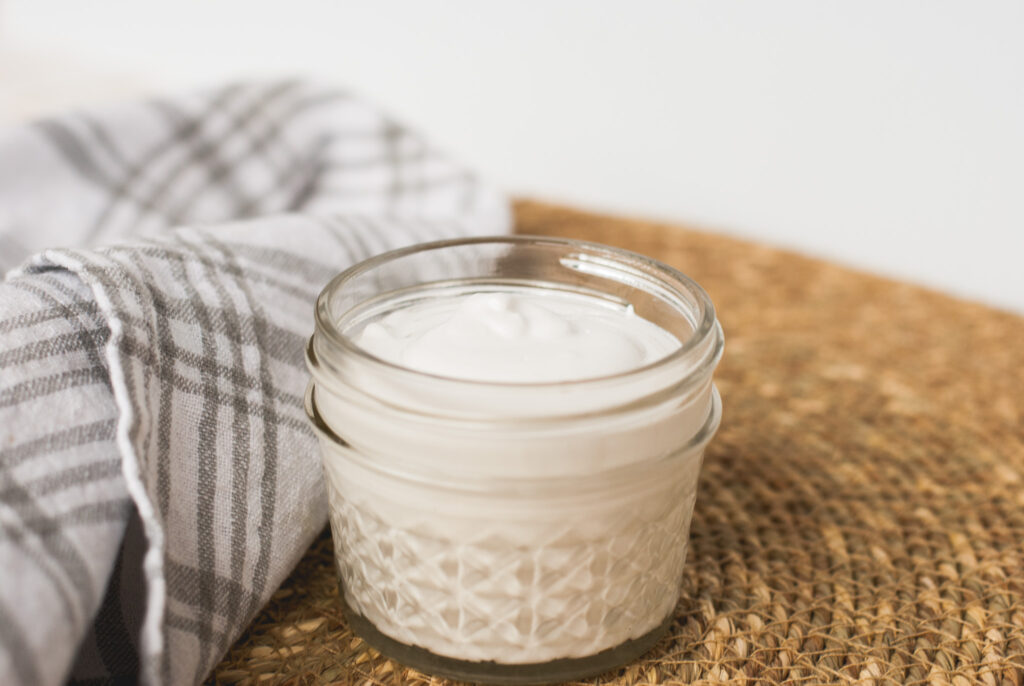 glass container of lotion on a brown mat. 