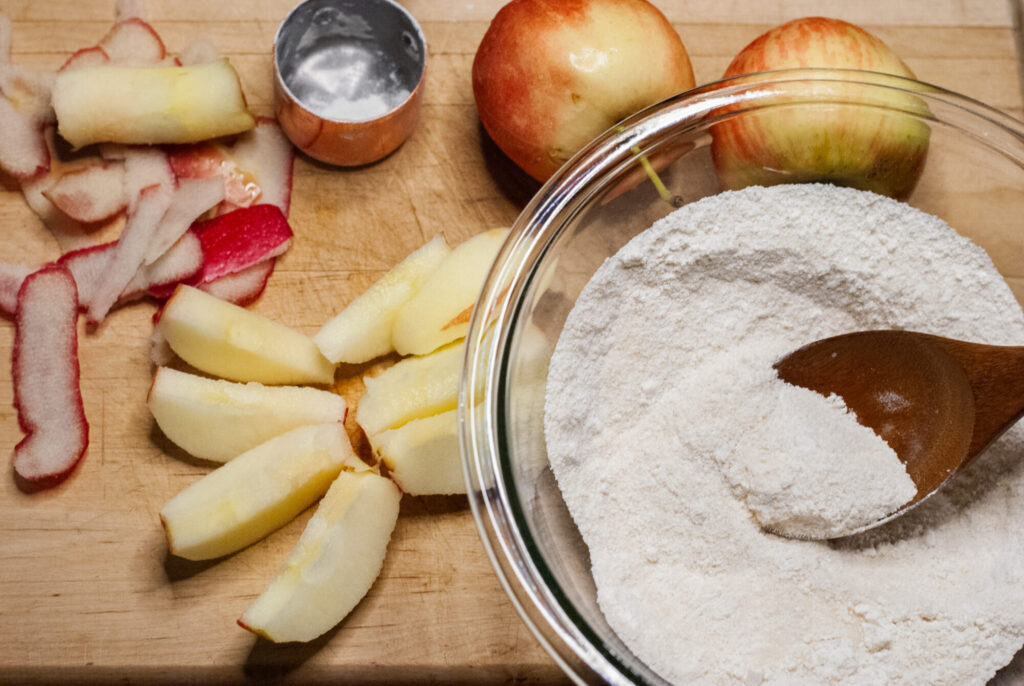 flour, sliced apples and apples on a cutting board 