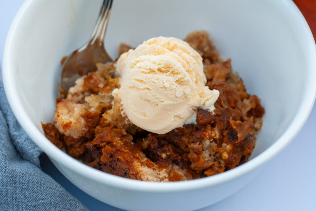 Pumpkin cobbler recipe  in a bowl with vanilla ice cream and a spoon. 