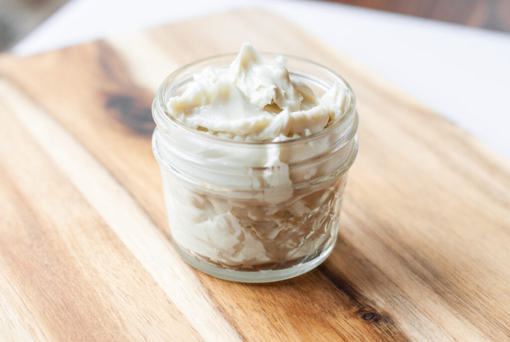 Whipped magnesium lotion in a glass container on a counter top. 