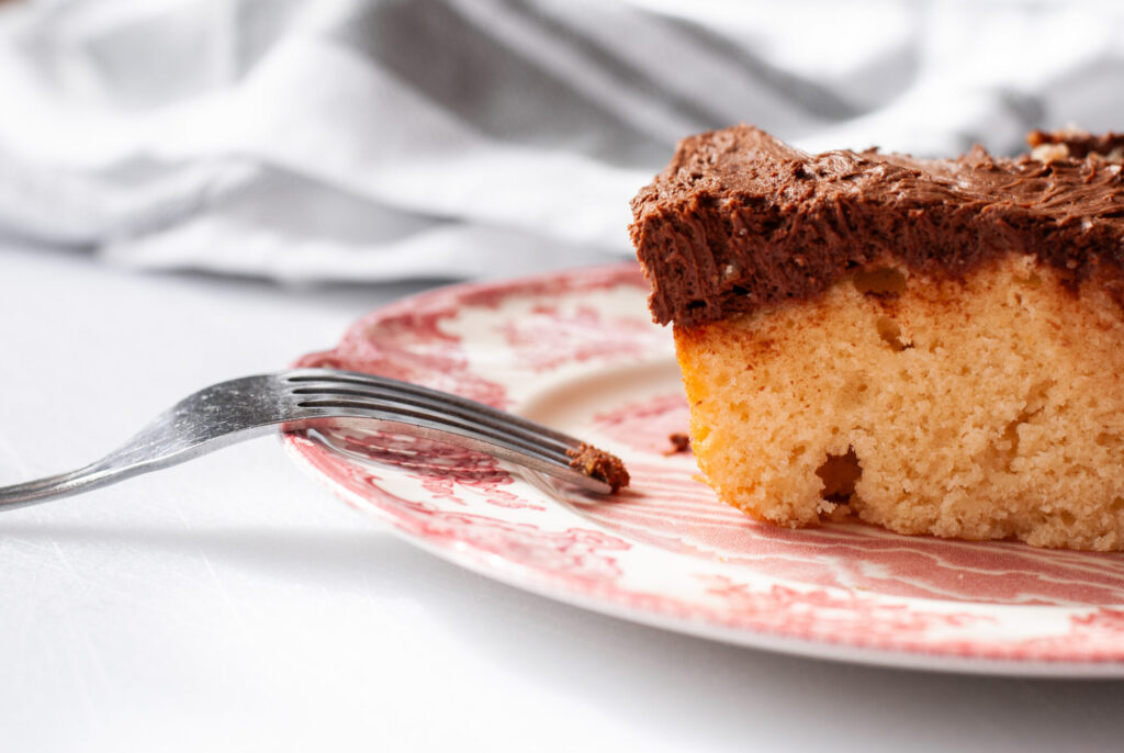 Yellow cake with chocolate buttercream frosting on a plate with a fork. 